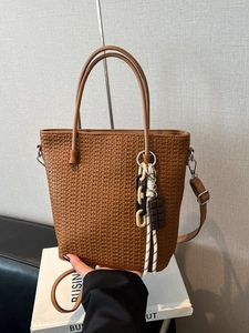 Brown woven bucket bag with double handles and decorative charms in a lifestyle setting