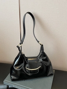 Retro black leather shoulder bag with gold crescent metal trim on a minimalist book setup