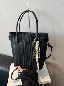 Black woven leather bucket tote bag with adjustable strap and decorative charm