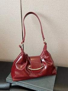 Deep red glossy leather hobo bag with a gold crescent buckle on a grey book background