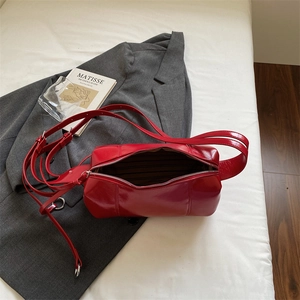 Rote glänzende Zylindertasche aus Leder auf grauem Anzug mit künstlerischer Deko
