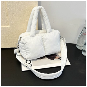 Detail shot of a white quilted puffer tote bag with padded handles on a black surface