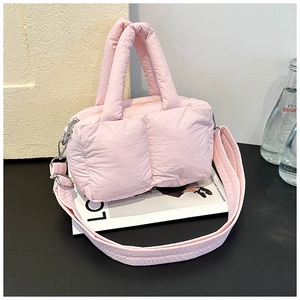 Pink quilted puffer bag with adjustable strap and top handle on a minimalist background