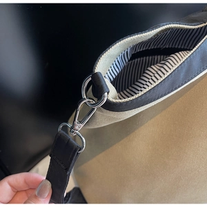 Detail of khaki canvas tote bag with black strap, silver hardware and striped lining