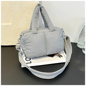 Detail of grey quilted puffy tote bag with wide shoulder strap on a black surface