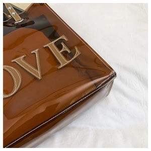 Detail der braunen PVC-Tasche mit weißen LOVE-Buchstaben und Leder-Nietenbesatz