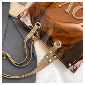 Detail der bernsteinfarbenen PVC-Tasche mit Lederriemen und silbernen Metallnieten