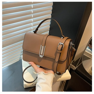 Detail of caramel leather handbag featuring a silver square buckle and top handle