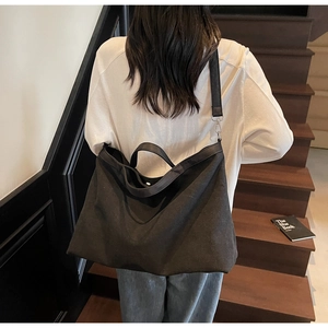Detail of a large black canvas tote bag showing reinforced handles and wide shoulder strap