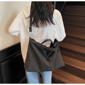 Detailed view of large black canvas tote bag worn by model on adjustable shoulder strap