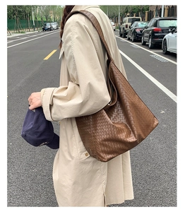 Outdoor street view of a large brown woven leather tote bag shown from a side-back angle