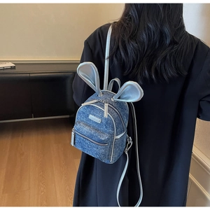 Detail view of mini blue denim backpack with silver rabbit ear design on model