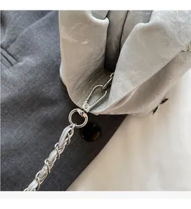 Close-up of polished silver-tone metal clasp and woven leather chain on the cloud bag