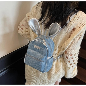 Detail of light blue denim backpack with shiny silver rabbit ears and front zipper pocket