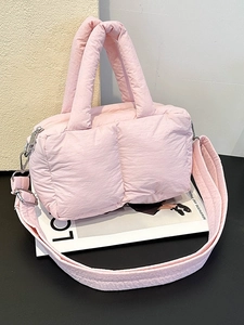 Pink quilted puffer tote bag with wide shoulder strap shown on a magazine background