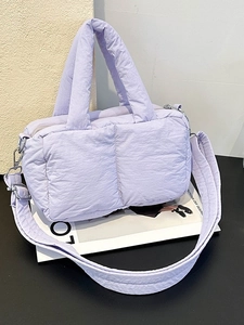 Quilted light purple puffer tote bag with thick handles and adjustable strap on a table