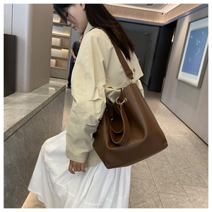 Close-up of a brown leather tote bag with a golden ring buckle and a wide shoulder strap