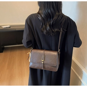 Détail d'un sac bandoulière marron vintage avec texture plissée et breloque en perles