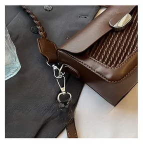 Detailed view of dark brown woven leather texture and silver metal lock on shoulder bag