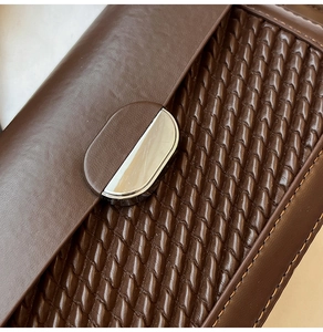 Close-up of dark brown woven leather underarm bag with silver semi-circular metal lock