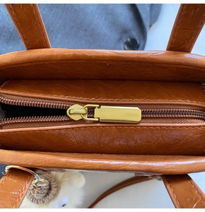 Close-up of brown textured PU leather bucket bag with gold zipper and plush charm detail