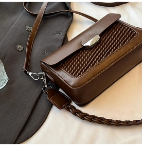 Close-up of deep brown woven shoulder bag with silver clasp on a grey suit jacket
