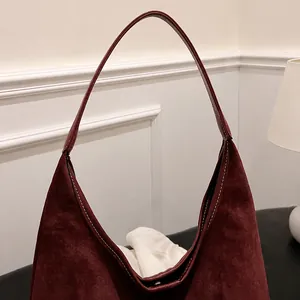 Detalle del bolso de hombro en cuero esmerilado burdeos con costuras finas sobre fondo blanco