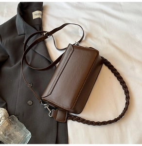 Detailed view of a brown leather shoulder bag with woven handle and adjustable strap
