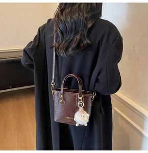 Detail of dark brown glossy crocodile texture bucket bag with plush charm and gold hardware