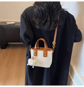 Detail of white bucket bag with brown trim and plush ball charm on a model