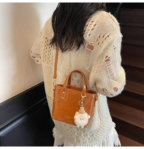 Detail view of caramel brown crossbody bucket bag with plush sheep charm accessory