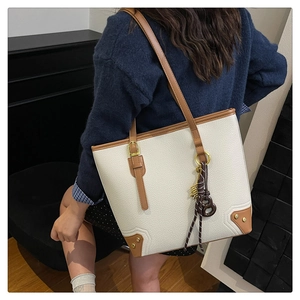Detail of cream pebbled leather tote with brown straps and retro decorative pendant