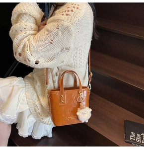 Detail of glossy wrinkled leather bucket bag with plush charm on a wooden stair