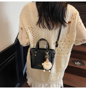 Detail of black glossy bucket bag with adjustable strap and white plush charm on stairs