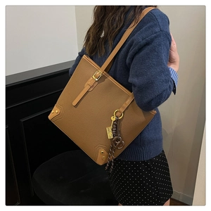 Close-up of brown textured leather tote bag with gold hardware and decorative charms