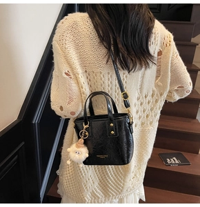 Detail of black glossy handbag with gold rivets and cute white lamb doll pendant