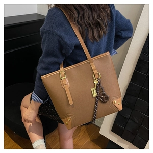 Detail of brown faux leather tote bag featuring a pretzel charm and gold key tag