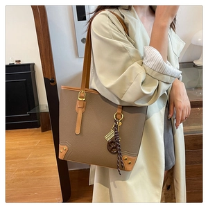 Detailed view of brown textured leather tote bag with stylish charms worn by a model