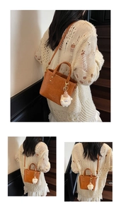 Detail view of brown vintage bucket bag with gold rivets and white plush doll charm