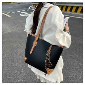 Detail of black pebbled leather tote with tan straps and gold rivets at bottom corners