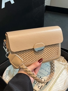 Khaki woven flap shoulder bag with silver buckle held by a hand in a stylish scene