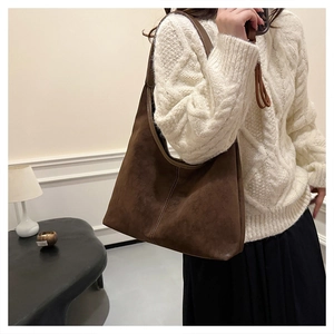 Detalle del bolso hobo de ante marrón con costuras verticales en un conjunto de otoño