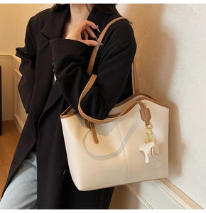 Detail of off-white tote bag with brown handles and a cute elephant charm on a model