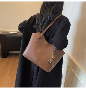 Detail of a brown leather tote bag with gold buckle, bow charm and Fashion trend text