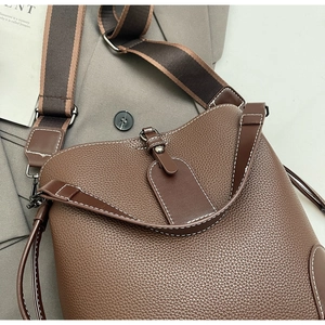 Detail of dark brown pebble leather bucket bag with white stitching and woven strap