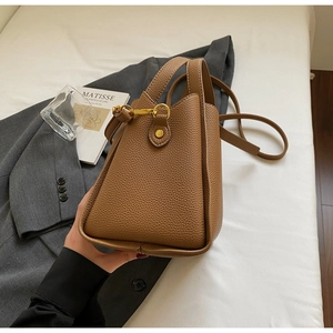 Dettaglio di una borsa a secchiello in pelle marrone motivo litchi con fibbie dorate