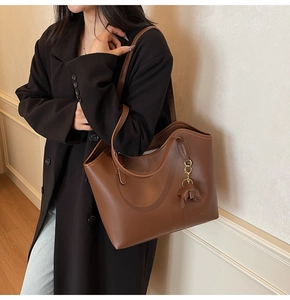 Detail of brown faux leather tote bag featuring a cute elephant charm and slim straps