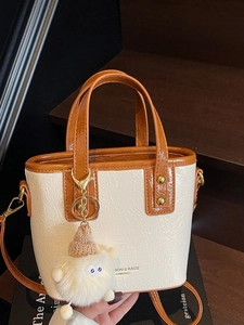 Cream and brown mini bucket bag with pleated texture and plush charm on wooden stairs