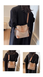 Detail view of beige lychee leather bucket bag with brown contrast trim and wide strap