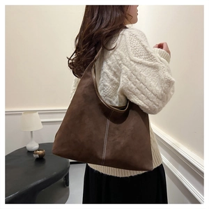 Detalle de bolso tote de ante mate marrón oscuro con costuras blancas en la correa de hombro
